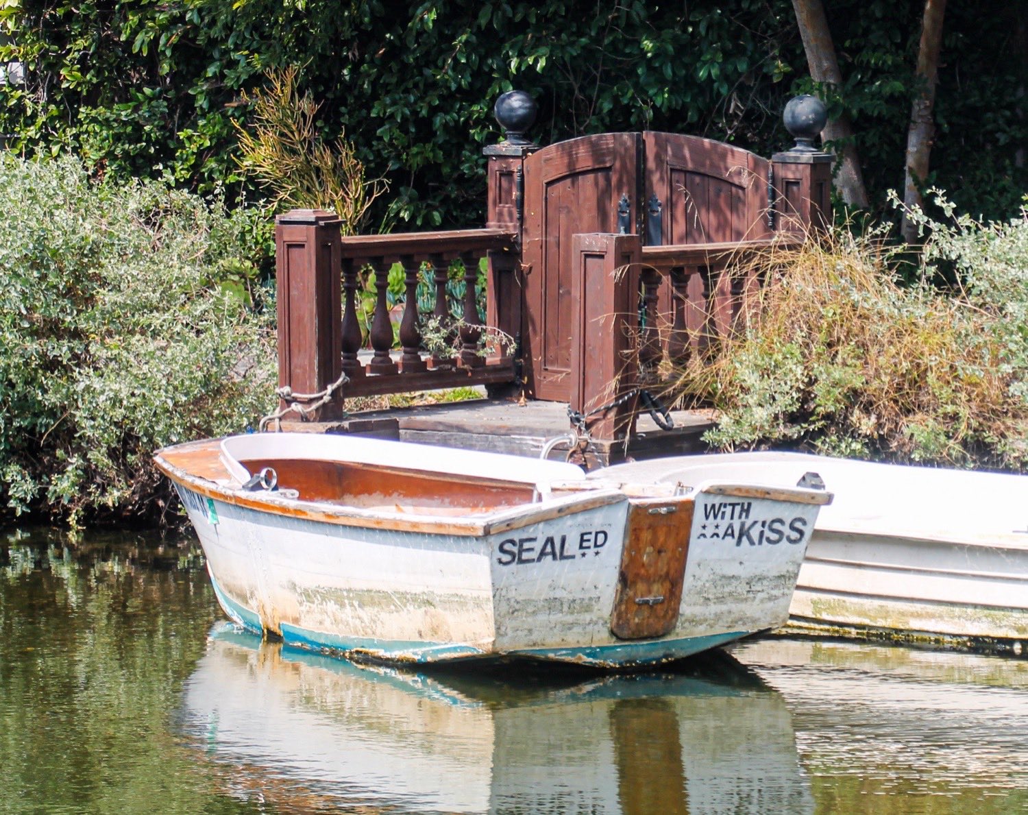 A weathered rowboat named Sealed With A Kiss moored on a canal