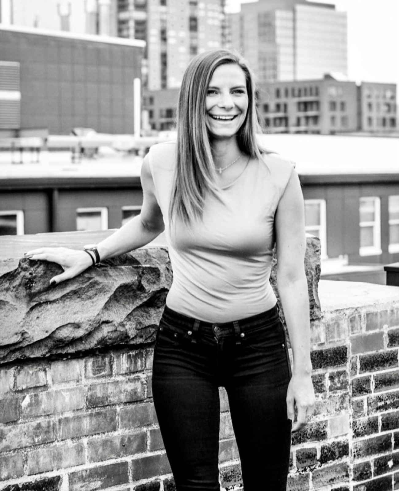 Kate laughing on a downtown rooftop, city skyline behind her