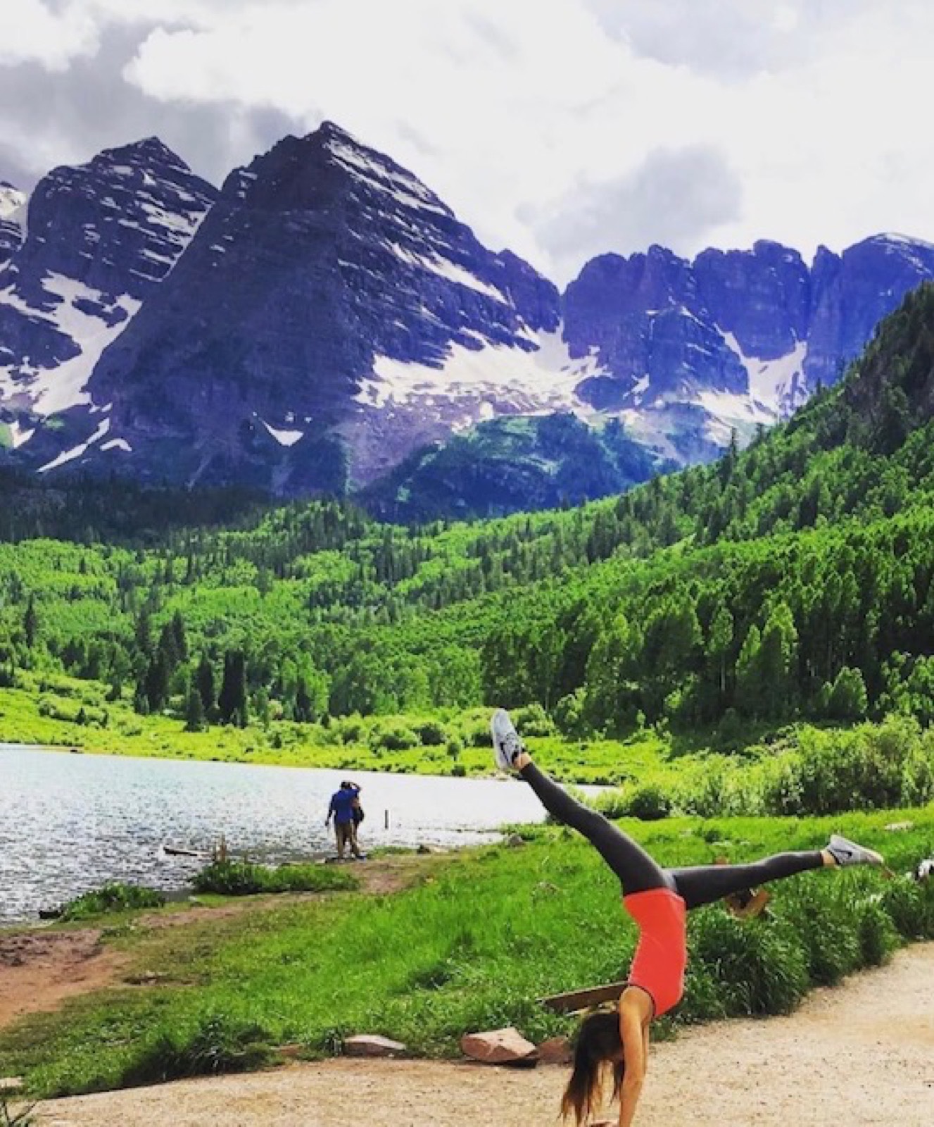 Kate doing a one-armed handstand beside an alpine lake in the mountains